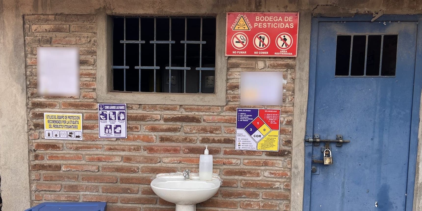 Bodega de plaguicidas con letreros de prohibición, rombo de peligros, lavamanos con jabón y puerta cerrada con candado
